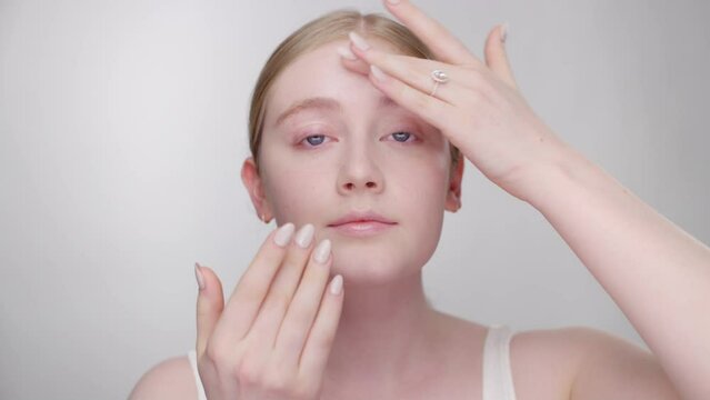 Makeup Tutorial: Blonde model gently applies primer to face with fingers
