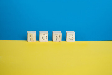 Wooden cubes arranged horizontally on blue and yellow background. Conceptual, symbolic image of the colors of the flag of Ukraine with the keyword hope.