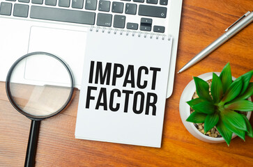 IMPACT FACTOR text on paper with laptop, green plant and pen