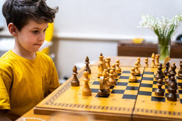 Brunette boy playing a game of chess on large chess board at home.