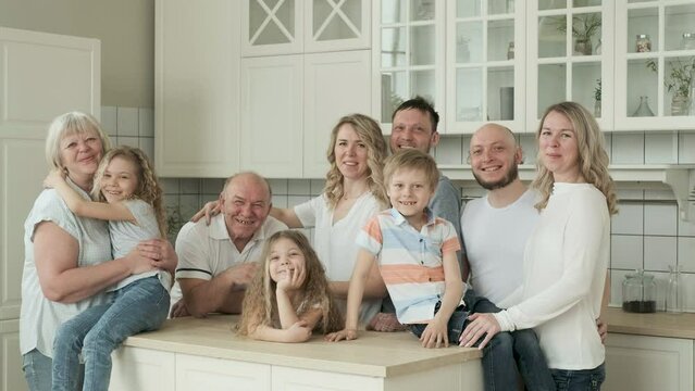 Big happy Caucasian family of three generations gathered together in kitchen at home, talking, laughing. Grandma and grandpa are playing with grandchildren. Parents and children spend time together