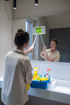 Young woman cleaning mirror in the bathroom