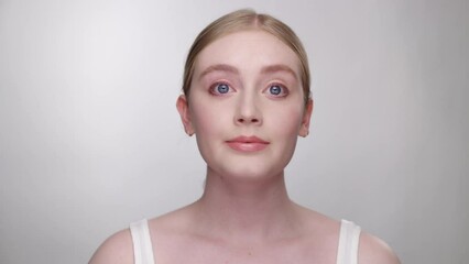 Beautiful blonde model looks into camera as she admires her makeup in mirror