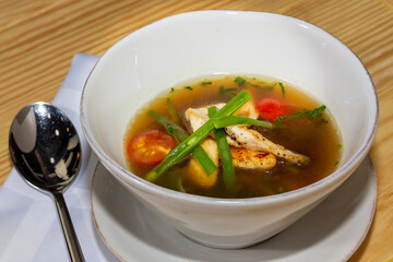 Chicken soup with vegetables in white bowl. Grey stone background.