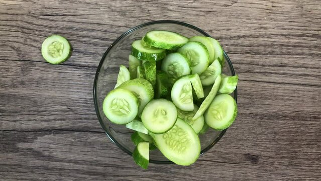 Close up hands put fresh food cucumbers in plate. Cooker cutting fresh cucumber into slices and adding it into bowl with salad