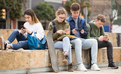Teens using phones outdoors, concept of youth obsession with social networks