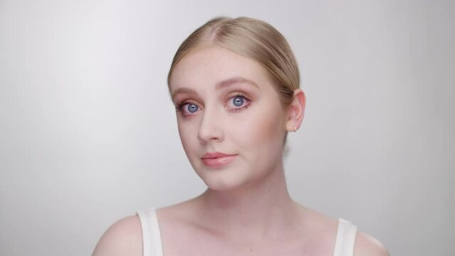 Striking blonde model evaluates her appearance in mirror, looking into camera