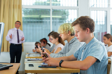 Group of teenage students using smartphones in classroom at school