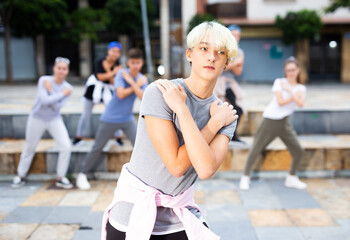 Confident teenager street dancer posing during performance with group in summer city .