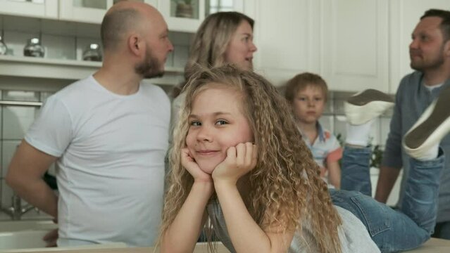 Portrait of little girl in kitchen smiling. Happy childhood. Caucasian girl with long curly hair looks at camera inside apartment and laughs