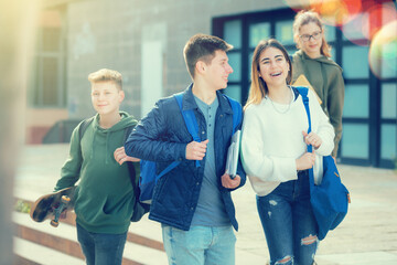 Group of smiling teen pupils walking after lessons outdoors at warm spring day