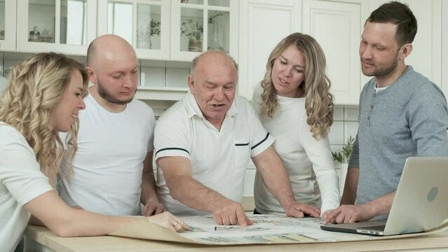 Large family of three generations of relatives in kitchen together discussing project of buying and repairing house or apartment. on table is drawing of layout of rooms and Parking