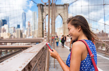 New York tourist woman using phone app walking on Brooklyn Bridge towards Manhattan city skyline....