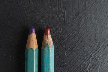 close up de puntas de dos lápices de color rojo carmín y morado desgastadas sobre fondo negro de...