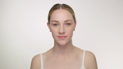 Pretty blonde model in tank top looks intently to camera against white backdrop