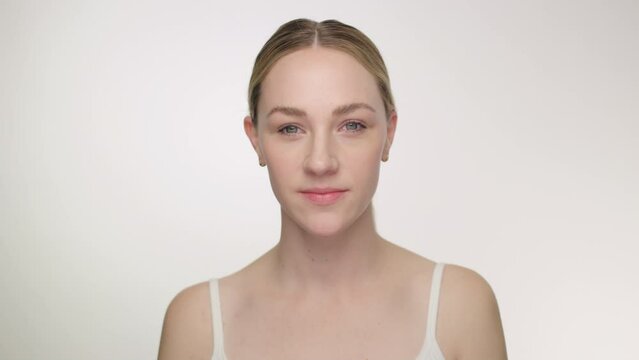 Pretty blonde model in tank top looks intently to camera against white backdrop