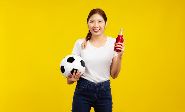 Happy Young Asian woman over isolated yellow background holding a soccer ball and drinks, sport and people concept