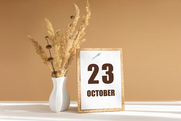 october 23. 23th day of month, calendar date.White vase with dried flowers on desktop in rays of...