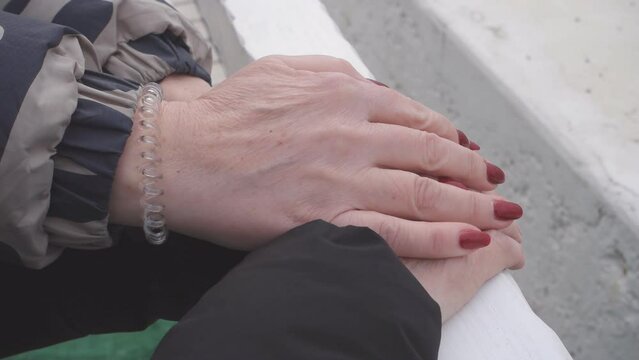 A woman with painted nails puts her hands on the hands of another elderly woman.