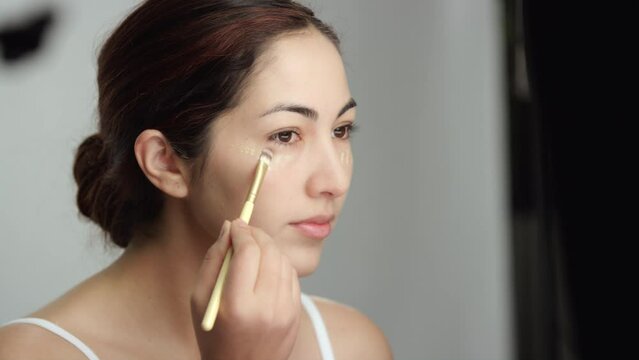 Makeup tutorial: Side view of brunette model brushing in liquid foundation