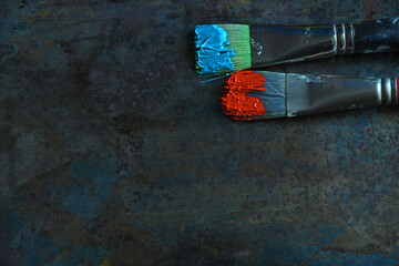 Two horizontal paint brushes with bright colored oil paints on bristles on grey background and copy...