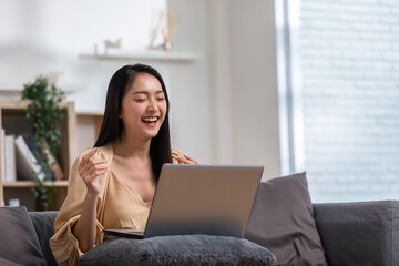 beautiful asian young woman wear casual sit on couch using computer laptop entertain with social media relax smile and laughing.Freelance woman working online sale marketing,Shopping online at home.