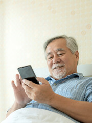 Senior Male using a smartphone , smiling feel happy in bed at home - lifestyle senior concept