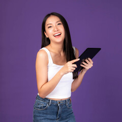 Beautiful Asian brunette woman cute girl in white tank top playing a smart phone , tablet computer isolated on purple background - mobile phone uses a online banking for pay online shopping