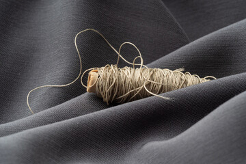 A spool with beige threads in a draped soft gray fabric, close-up, macro. Atelier, tailoring,...