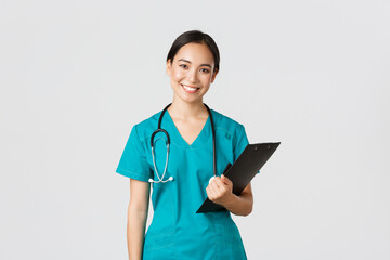 Healthcare workers, preventing virus, quarantine campaign concept. Smiling asian female nurse, doctor with clipboard wearing scrubs, provide checkup, examine patient in clinic, white background - Powered by Adobe