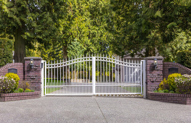 Iron front gate of a luxury home. Wrought iron white gate and brick pillar - obrazy, fototapety, plakaty