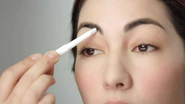 Makeup tutorial: extreme closeup of eyebrow pencil being used by brunette model