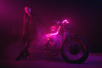 Naklejka na ściany i meble Girl a motorbiker near the old motorcycle in the neon lights.