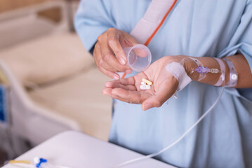 Patient woman hands pouring pills from a cup on to hand at hospital