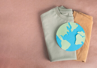 Recycling clothes concept. T shirts and papercraft planet Earth on natural background. Environment...