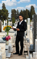 Bearded Jew in black kippah reading a Hebrew Bible, praying. Prayer in a jewish cemetery in Israel. Judaic Tombstones with shallow depth of field. Selective focus. Old jewish cemetery in the forest.
