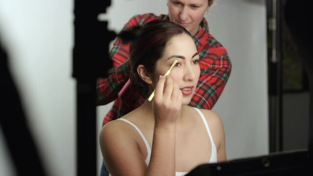 Behind the scenes photo shoot model touches up makeup as hairstylist fixes hair