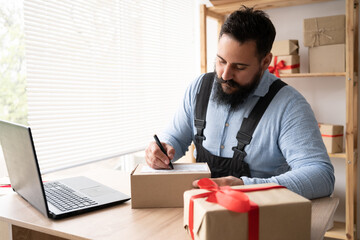 Indian male business owner working from home online shopping Concept of entrepreneur and online trading. Sitting at home in workplace with a laptop in work overalls and writes the delivery address.