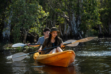 Asian attractive romantic young couple rowing kayak in a forest lake.  - obrazy, fototapety, plakaty