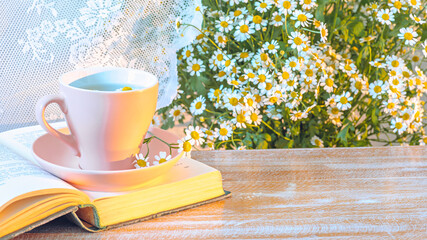 Chamomile tea, open book and bouquet on a bench by the window