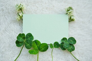 白い布の背景に二つ葉、三つ葉、四つ葉と五つ葉のクローバーと花を飾った緑のカードのタイトルスペース