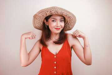 Gorgeous strong young Asian woman with orange dress and straw hat showing biceps and smiling....