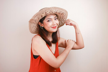 Gorgeous strong young Asian woman with orange dress and straw hat showing biceps and smiling....