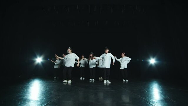 The youth team performs on stage with hip hop. Young people are dressed in white T-shirts and black pants. They make movements in sync