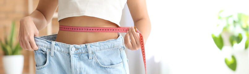 Young woman in loose jeans measuring waist at home. Diet concept