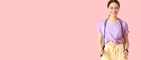Sporty young woman holding skipping rope on pink background with space for text