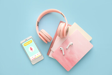 Mobile phone with word PODCAST on screen, headphones, notebooks and earphones on color background