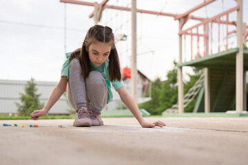 Girl draws with colorful crayons on pavement. Children's drawings with chalk on wall. Creative kid. Joy of childhood