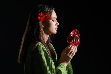 Young woman with wet hair holding bouquet of beautiful anthurium flowers on dark background