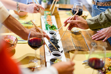 Friends with chopsticks eating Asian food and drinking red wine